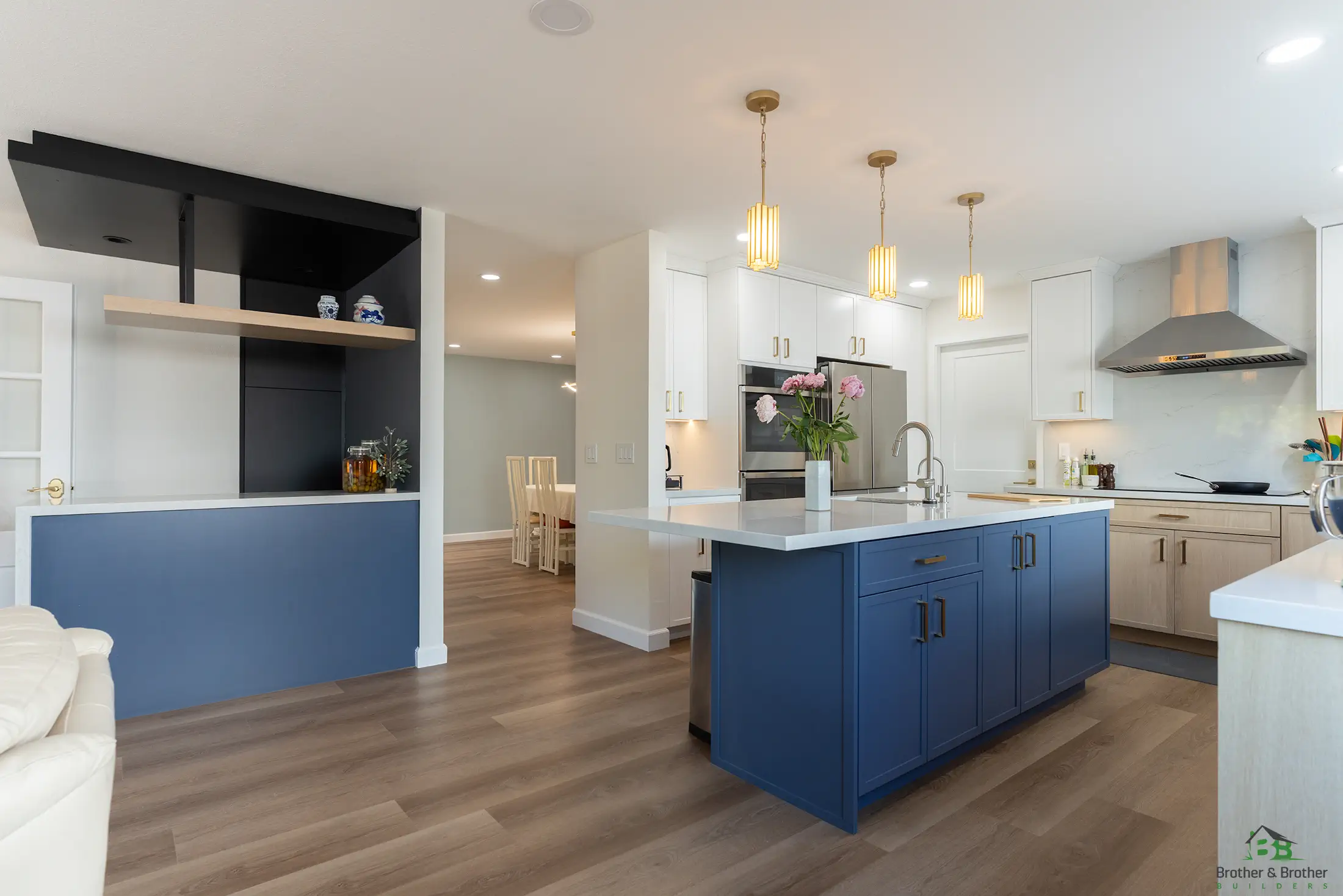 Open-concept kitchen remodeling by Brother & Brother Builders featuring a navy island, gold pendant lighting and quartz countertops